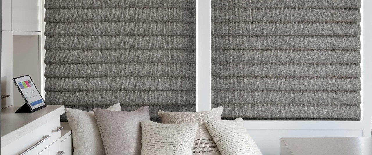 Tan pillows in front of grey, closed roman shades
